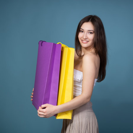 Happy young woman shopaholic with shopping bags at sale time, isolated on blue backgroundの写真素材