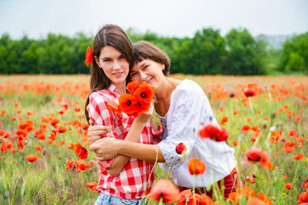 Attractive middle-aged woman have fun on a poppy field with her daughter, summer outdoor.の写真素材