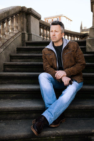 Urban outdoor portrait of a handsome man wearing blue jeans and brown jacket, street style at springの写真素材
