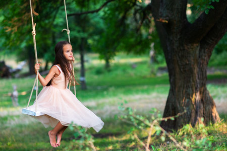 Happy girl rides on a swing in park. Little Princess has fun outdoor, summer nature outdoor. Childhood, child lifestyle, enjoyment, happiness.の写真素材