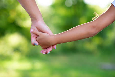 Mother leads her kid in summer forest nature outdoor. Trust, family, protection and help concept. Female and child's hands closeup against the background of summer greenery. Parent walks with daughter in parkの写真素材
