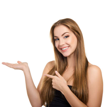 Young attractive woman with perfect make-up and long fair hair smiling and pointing with her hands at copy space at studio over white background, beauty female portrait.の写真素材