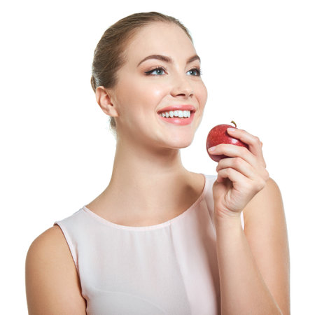 Young attractive woman posing at studio with perfect smile holding red apple over white background.の写真素材