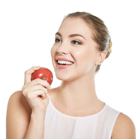 Young attractive woman posing at studio with perfect smile holding red apple over white background.の写真素材