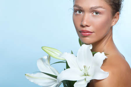 Portrait of a beautiful young woman with clean skin, soft day makeup and white lilies flowers, beauty treatment, cosmetology and anti-aging themeの写真素材
