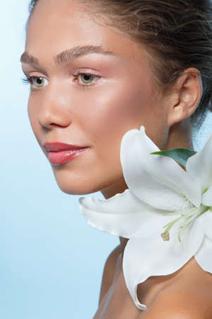 Portrait of a beautiful young woman with clean skin, soft day makeup and white lilies flowers, beauty treatment, cosmetology and anti-aging themeの写真素材