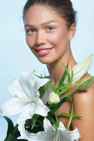 Portrait of a beautiful young woman with clean skin, soft day makeup and white lilies flowers, beauty treatment, cosmetology and anti-aging themeの写真素材