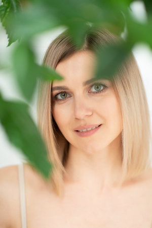Beautiful calm middle aged woman with green plant, natural light. Anti-aging and beauty treatment.の写真素材