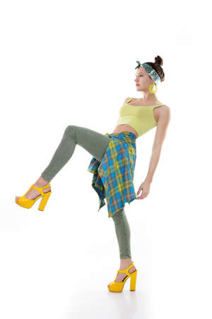 Young fashion charming girl wearing streetwear and yellow high heel sandals dancing at studio on a white backgroundの写真素材