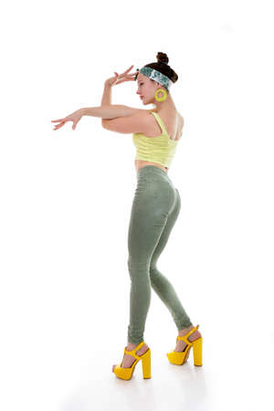 Young fashion charming girl wearing streetwear and yellow high heel sandals dancing at studio on a white backgroundの写真素材
