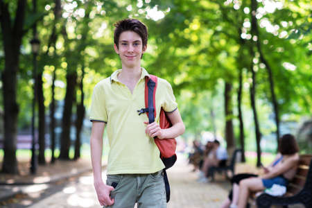 Young handsome 15 years old teen boy wearing yellow t-shirt with backpack looking at camera and happy smiling, summer park outdoorの写真素材