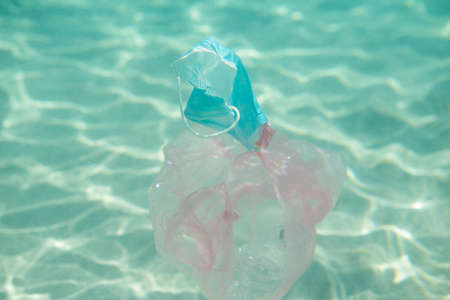Ocean pollution. Personal protective mask, plastic bottle and bag underwater. Consequences of...