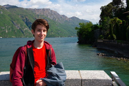 Handsome teen boy walking along promenade on Lake Como with great view at landscape with Alps mountains, beauty in nature at springtime, Italy, Lombardyの写真素材