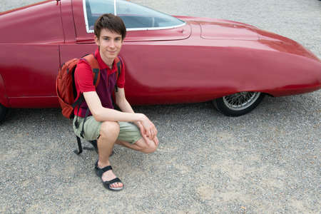 Handsome cheerful teen boy near retro racing red car outdoor, detail