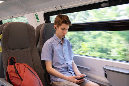 Handsome cheerful teen boy riding a train and using a smartphoneの写真素材