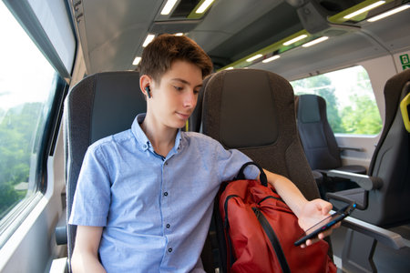 Handsome cheerful teen boy riding a train and using a smartphone