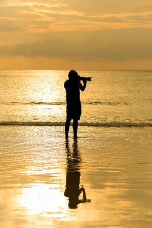 Man photographer act shooting with landscape sea sunset backgroundの写真素材