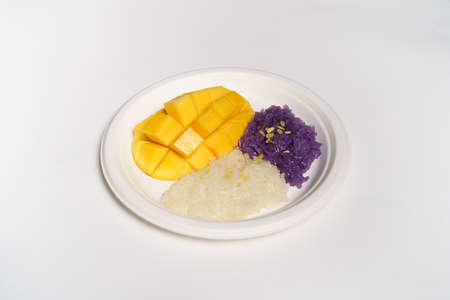 Thai Mango sticky rice on a white paper plate on a white background, topped with coconut milk.の写真素材