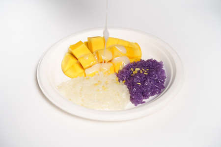 Thai Mango sticky rice on a white paper plate on a white background, topped with coconut milk.の写真素材