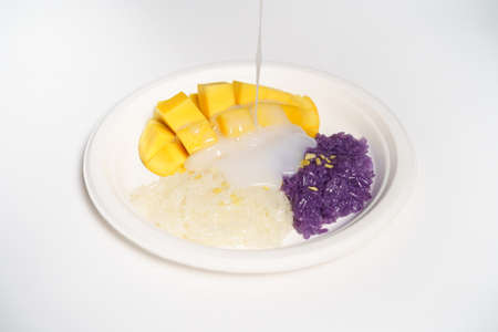 Thai Mango sticky rice on a white paper plate on a white background, topped with coconut milk.の写真素材