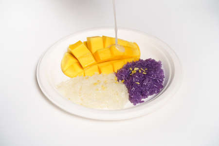 Thai Mango sticky rice on a white paper plate on a white background, topped with coconut milk.の写真素材