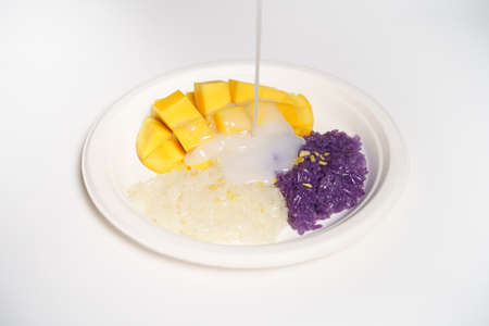 Thai Mango sticky rice on a white paper plate on a white background, topped with coconut milk.の写真素材