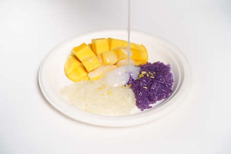 Thai Mango sticky rice on a white paper plate on a white background, topped with coconut milk.の写真素材