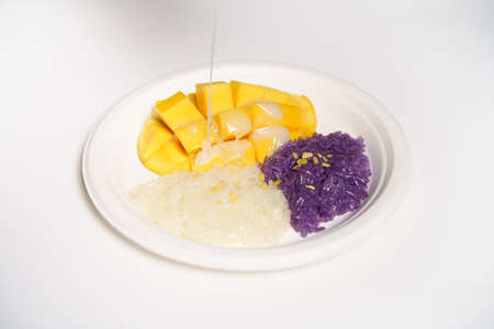 Thai Mango sticky rice on a white paper plate on a white background, topped with coconut milk.の写真素材