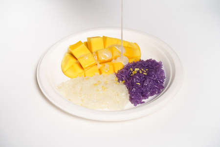 Thai Mango sticky rice on a white paper plate on a white background, topped with coconut milk.の写真素材