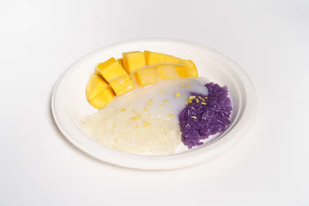 Thai Mango sticky rice on a white paper plate on a white background, topped with coconut milk.の写真素材