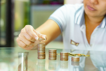 Saving money, woman stacking coins into increasing columns.