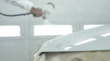 Process of painting a white car in a spray booth. Man using a spray gunの写真素材