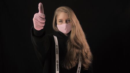Girl in a pink mask and a ribbon with the inscription covid 19 shows the gesture of approval....