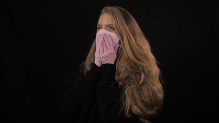 Girl in pink medical mask coughs. Isolated on black background. Health care and medical concept. Close up portrait . 4k. Coronavirus Epidemic, illness, pandemicの写真素材