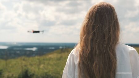 Girl in a white shirt and long hair stands with his back and a flying drone in the backgroundの写真素材