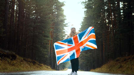 Girl holds the flag of United Kingdom in hands on the roadの写真素材