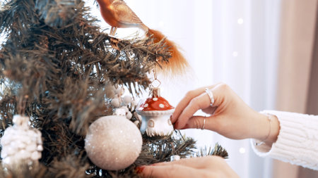 Female hands decorate christmas tree with toys at home. Beautiful mushroomの写真素材