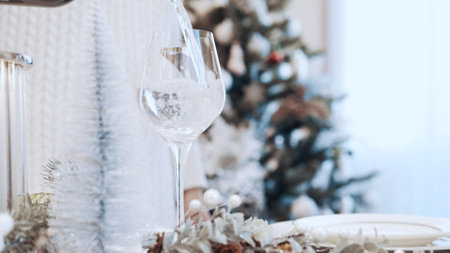 A girl in a white dress pours white wine into a glass. Christmas beautiful canned table
