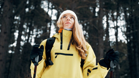 Girl with a white hat in the forest with a backpack and hiking sticks in winter. Front view. Close...