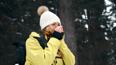 A girl in a white hat and a yellow anorak warms her hands in the winter in the forestの写真素材
