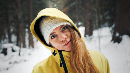 Girl in a yellow jacket and a hoodie smiles looking forward in the winter in the forestの写真素材