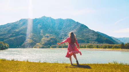 Lady in long red dress overlooks the edge of two rivers with mountains on the background. Drone footageの写真素材