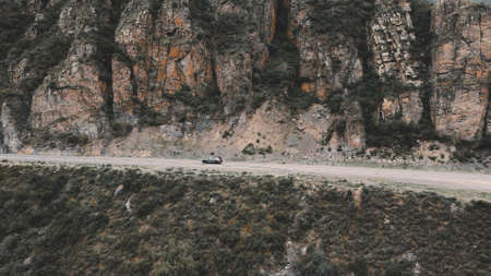 Dark grey car drives through narrow road in the mountains. Drone footageの写真素材