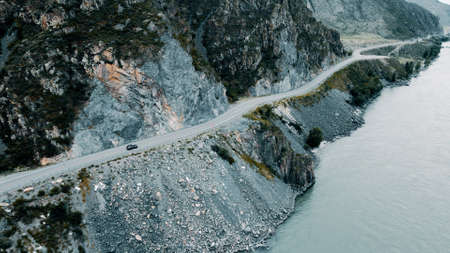 Dark grey car drives through narrow road in the mountains. Drone footageの写真素材
