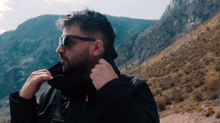 A man with glasses sits on the edge of a cliff wearing a black anorak. Katu-Yaryk canyon Chulyshman Valley. Altaiの写真素材