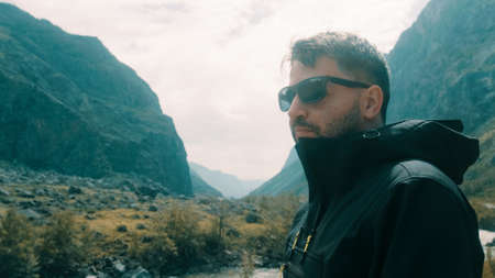 A man with glasses sits on the edge of a cliff wearing a black anorak. Katu-Yaryk canyon Chulyshman Valley. Altaiの写真素材