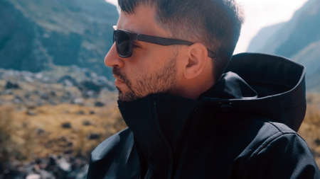 A man with glasses sits on the edge of a cliff wearing a black anorak. Katu-Yaryk canyon Chulyshman...