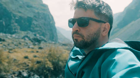 A man with glasses sits on the edge of a cliff wearing a green anorak. Katu-Yaryk canyon Chulyshman...