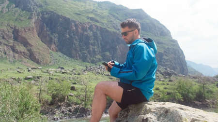 A man with glasses sits on the edge of a cliff wearing a blue anorak. Katu-Yaryk canyon Chulyshman...