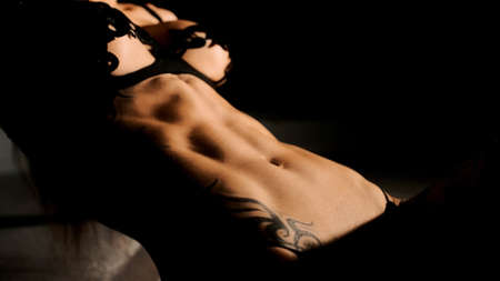 A girls sexy body under harsh lighting. Sexy underwear. Athletic physique. Black background. Close upの写真素材